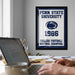 A framed poster of Penn State University from 1986 hangs on a wall, with a laptop and a coffee mug on a desk in the foreground.