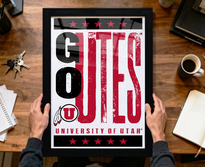 A framed poster with the text "GUES" and "UNIVERSITY OF UTAH" is being held by a person's hands.
