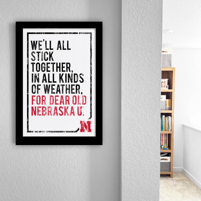 a framed quote on a wall, which reads "WE'LL ALL STICK TOGETHER, IN ALL KINDS OF WEATHER, FOR DEAR OLD NEBRASKA U."