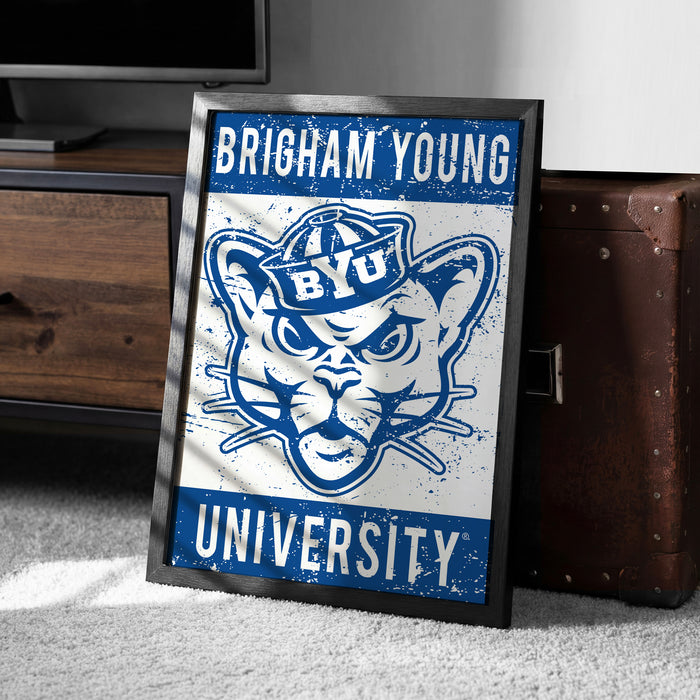 A framed poster with the text "BRIGHAM YOUNG" and "YU" is displayed on a carpeted floor next to a brown suitcase.