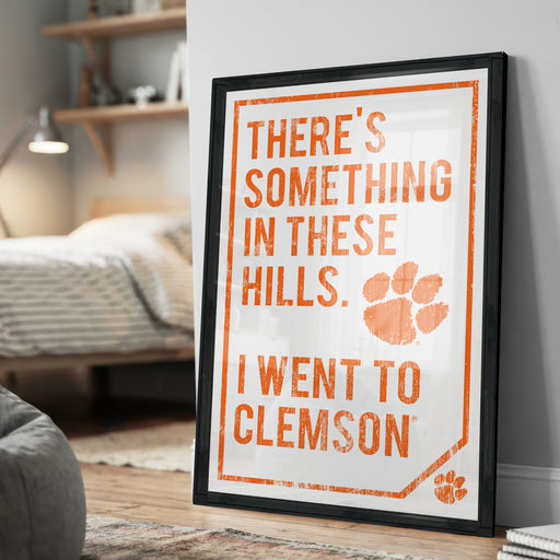 a framed poster with the text "There's something in these hills. I went to college" and an orange paw print symbol.