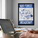 a framed poster of a bird, likely representing the Air Force Academy, hanging on a wall above a desk with a laptop and other office supplies.