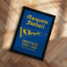 A framed poster with the text "Marquette Football" and "UNDEFEATED SINCE 1960" on a blue background, along with a yellow flag icon.