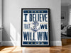 a framed poster with the text "I BELIEVE THAT WE WILL WIN" and an anchor symbol, placed on a wooden floor against a white wall.