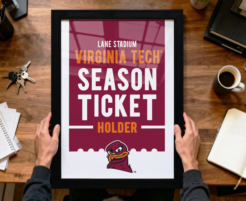A framed poster advertising a Virginia Tech football season ticket holder, with a person's hands holding the frame.