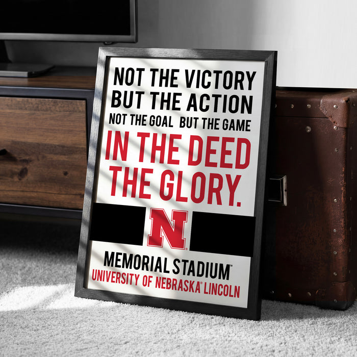 a framed sign with text that reads "NOT THE VICTORY BUT THE ACTION NOT THE GOAL BUT THE GAME IN THE DEED THE GLORY. MEMORIAL STADIUM UNIVERSITY OF NEBRASKA LINCOLN".