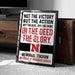a framed sign with text that reads "NOT THE VICTORY BUT THE ACTION NOT THE GOAL BUT THE GAME IN THE DEED THE GLORY. MEMORIAL STADIUM UNIVERSITY OF NEBRASKA LINCOLN".