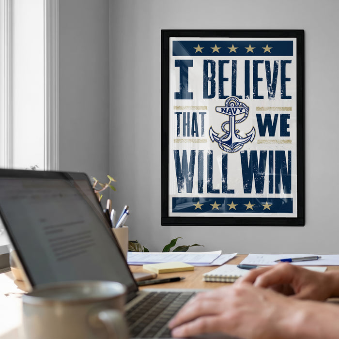 a framed poster with the text "I BELIEVE THAT WE WILL WIN" on it, which is displayed on a wall above a desk with a laptop and other items.