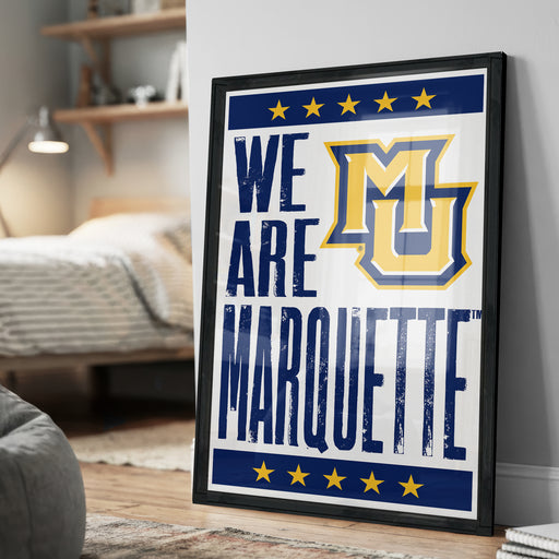 A framed poster with the text "WE ARE MARQUETTE" and a logo, placed on a wall in a bedroom.
