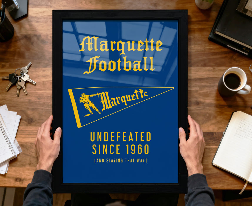 A framed poster with the text "Marquette Football" and a yellow flag, held by a person's hands.