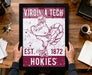 A framed poster featuring a turkey and the text "VIRGINIA TECH EST. 1872 HOKIES" is being held by a person's hands.