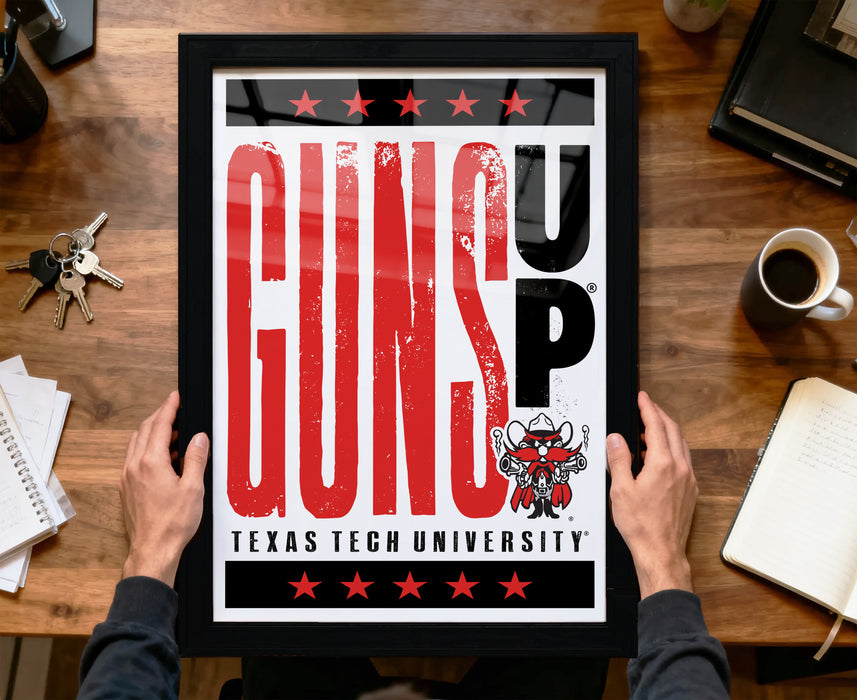 A framed poster with the text "GUNS UP" and a graphic of a character holding a gun, placed on a wooden desk.