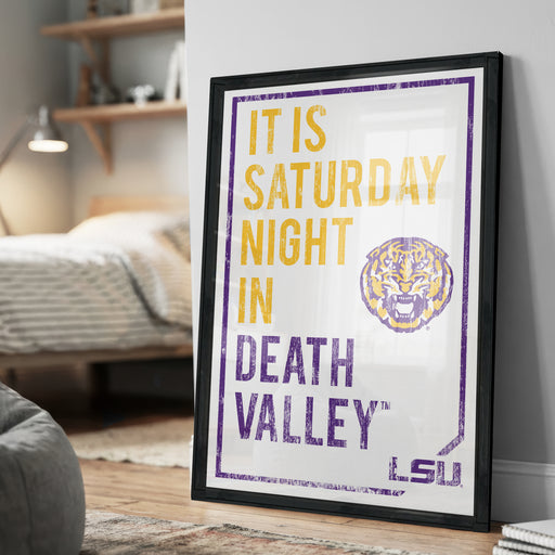 A framed poster with the text "IT IS SATURDAY NIGHT IN DEATH VALLEY" and a tiger logo, placed on a wall in a bedroom.