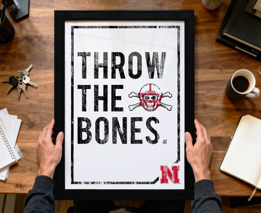 A framed poster with the text "THROW THE BONES" and a football helmet graphic is being held by a person's hands.