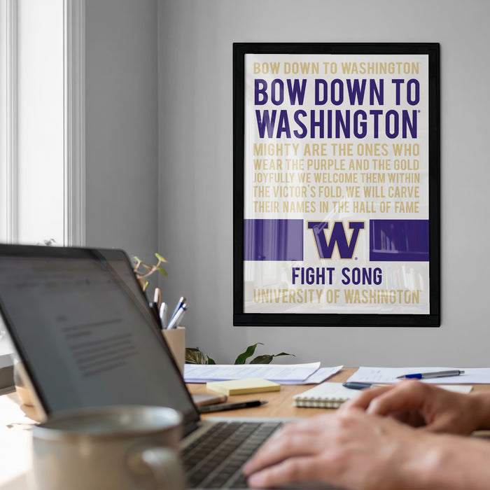 a framed poster with text on it, hanging on a wall above a desk with a laptop and other items on it.