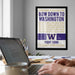 a framed poster with text on it, hanging on a wall above a desk with a laptop and other items on it.