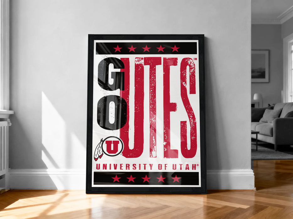 A framed poster with the text "GOUTES UNIVERSITY OF UTAH" displayed prominently on it, standing on a wooden floor against a white wall.