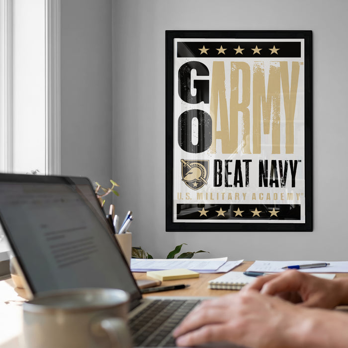 A framed poster with the text "GO ARMY BEAT NAVY" hangs on a wall above a desk with a laptop and other items.