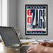 A framed poster with the text "GO ZAGS" hangs on a wall, with a laptop and various office supplies visible on a desk in the foreground.