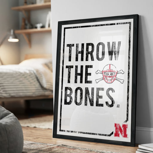 A framed poster with the text "THROW THE BONES" and a football helmet graphic, placed on a wall in a bedroom.