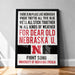 The image is a framed poster with text that reads: "THERE IS NO PLACE LIKE NEBRASKA WHERE THEY'RE ALL TRUE BLUE WE'LL ALL STICK TOGETHER IN ALL KINDS OF WEATHER FOR DEAR OLD NEBRASKA U. FIGHT SONG UNIVERSITY OF NEBRASKA LINCOLN"