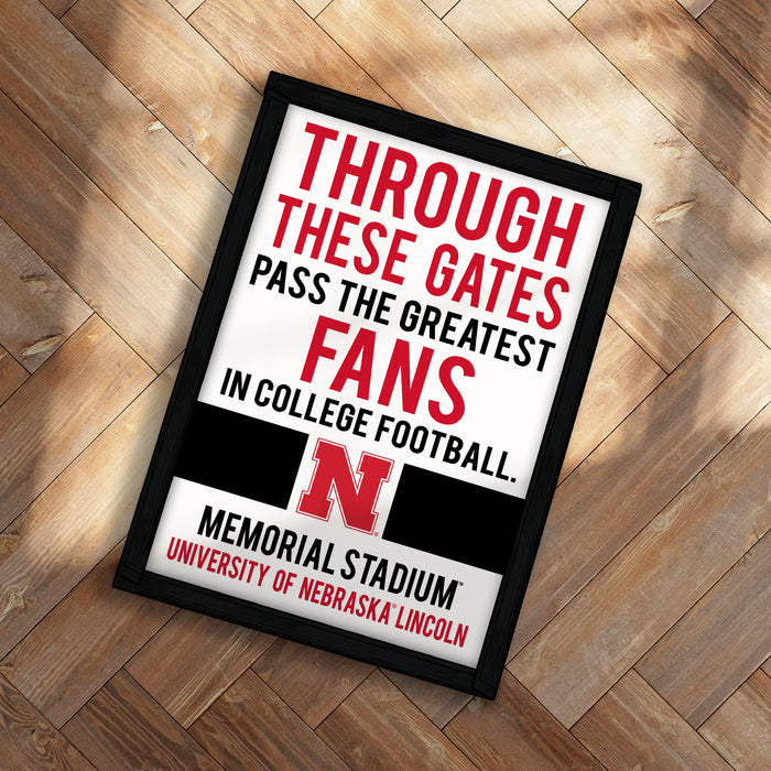 The image is a framed sign with text that reads "THROUGH THESE GATES PASS THE GREATEST FANS IN COLLEGE FOOTBALL. MEMORIAL STADIUM UNIVERSITY OF NEBRASKA LINDON".