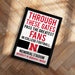 The image is a framed sign with text that reads "THROUGH THESE GATES PASS THE GREATEST FANS IN COLLEGE FOOTBALL. MEMORIAL STADIUM UNIVERSITY OF NEBRASKA LINDON".