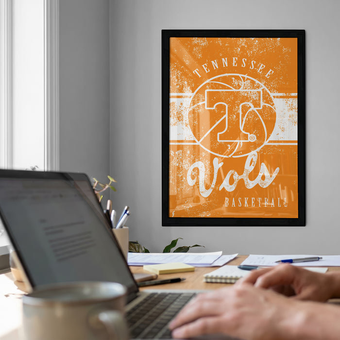 a person working on a laptop at a desk, with a framed poster of the Tennessee Titans basketball team hanging on the wall behind them.