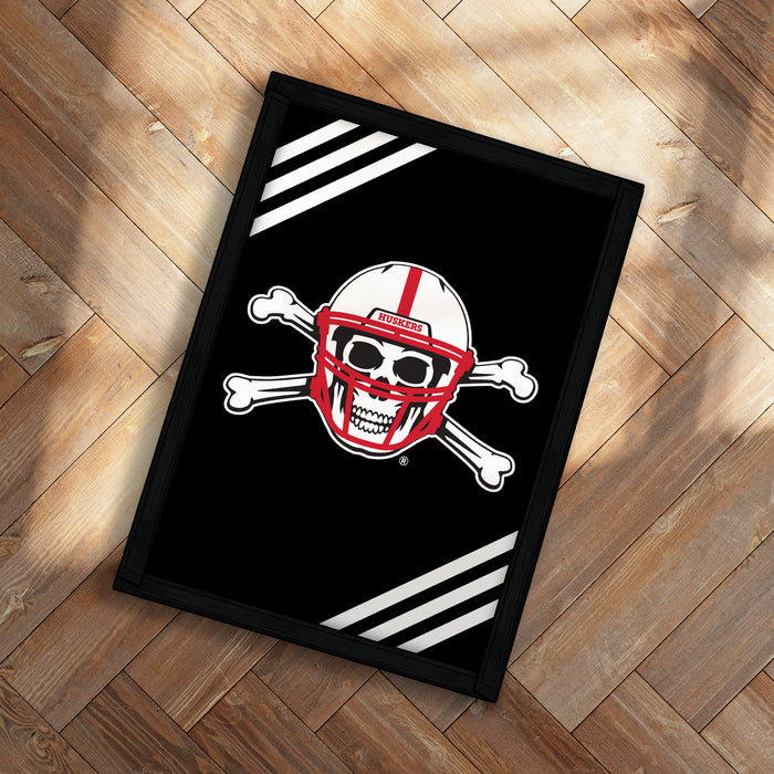 A framed poster with a skull and crossbones design on a black background, placed on a wooden floor.