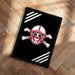 A framed poster with a skull and crossbones design on a black background, placed on a wooden floor.