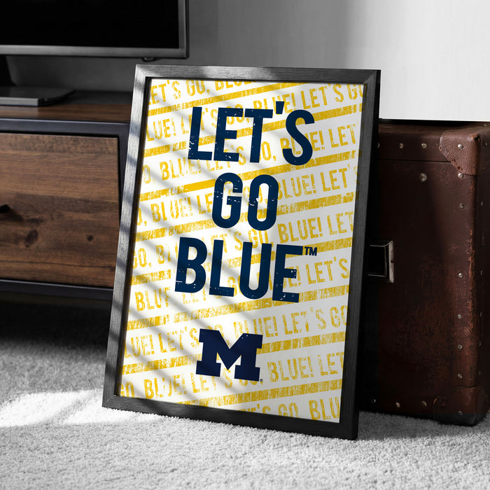 A framed poster with the text "LET'S GO BLUE™" printed on it, placed on a carpeted floor next to a wooden chest.