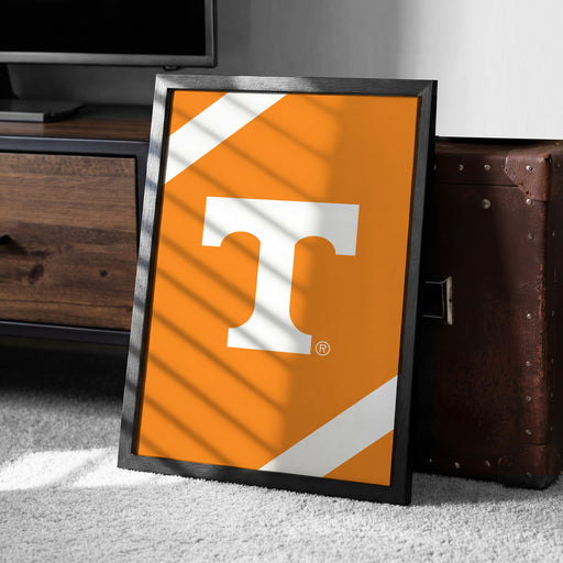 a framed poster with the letter "T" on it, placed on a carpeted floor next to a brown suitcase.