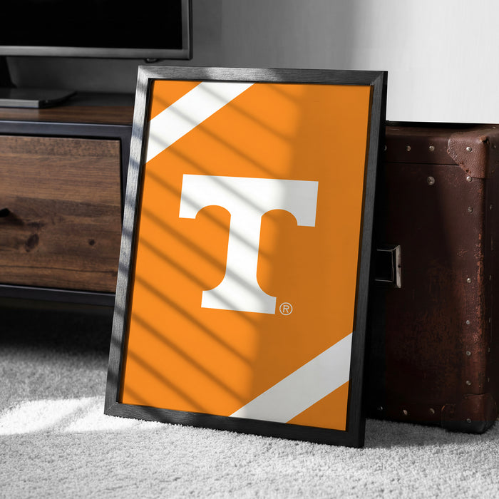 a framed poster with the letter "T" on it, placed on a carpeted floor next to a brown suitcase.