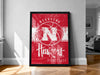 A framed poster of the Nebraska Huskies basketball team, featuring the team's logo and text, is displayed on a wall in a room.