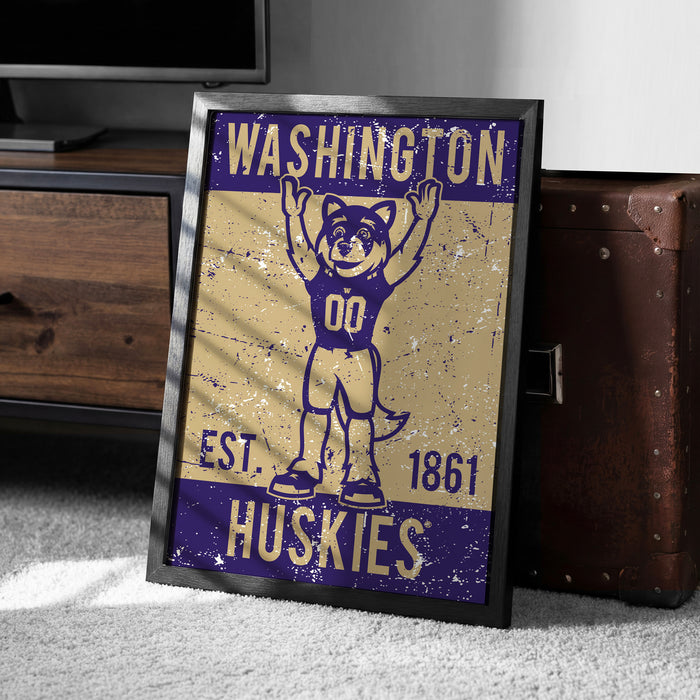 A framed poster featuring a cartoon character with the text "WASHINGTON EST. 1861 HUSKIES" on it, placed on a carpeted floor next to a wooden chest.
