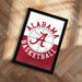 A framed poster with the Alabama basketball logo and text is displayed on a wooden floor.