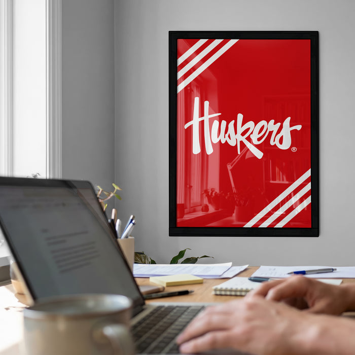 a workspace with a laptop computer, a framed poster of the word "Huskies" in red and white, and various office supplies on a desk.