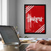 a workspace with a laptop computer, a framed poster of the word "Huskies" in red and white, and various office supplies on a desk.