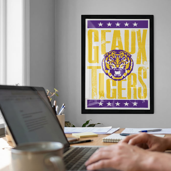 a framed poster of the LSU Tigers on the wall, with a laptop and a coffee cup on a desk in the foreground.
