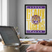 a framed poster of the LSU Tigers on the wall, with a laptop and a coffee cup on a desk in the foreground.