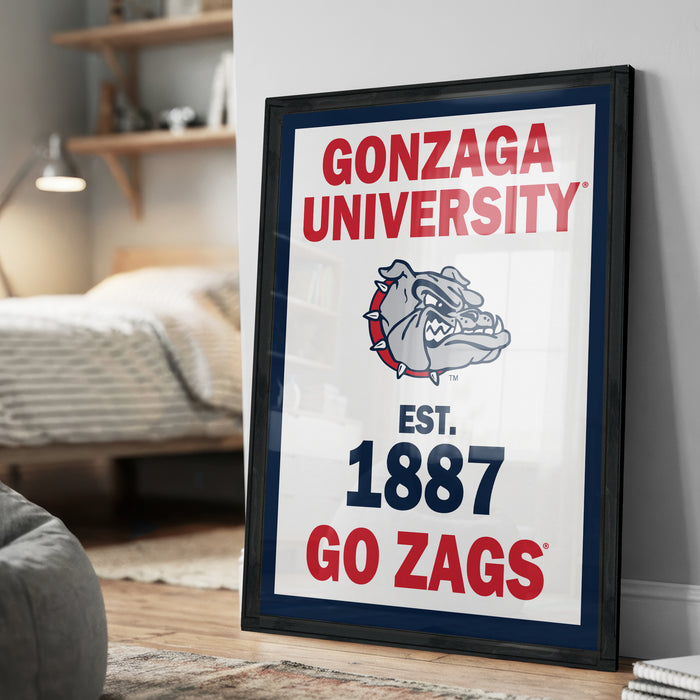 A framed poster with the text "GONZAGA UNIVERSITY EST. 1887 GO ZAGS" and a bulldog logo, placed on a wall in a bedroom.