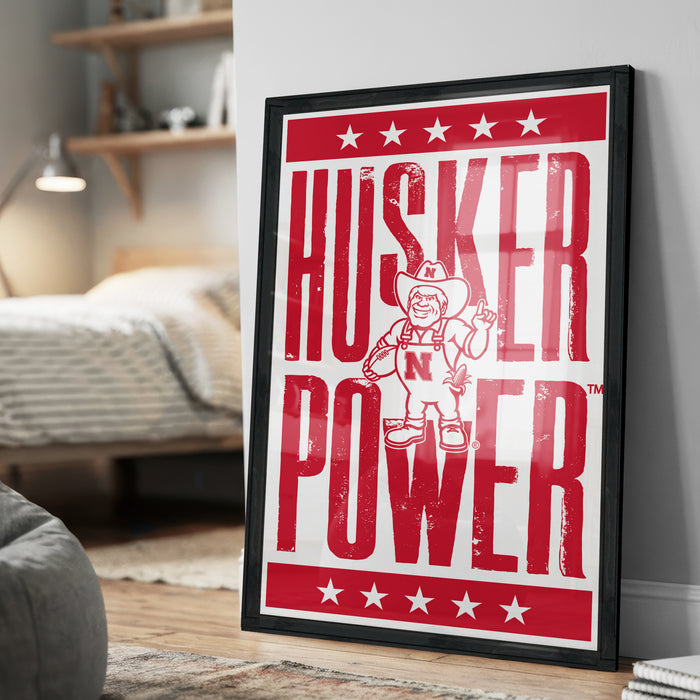 A framed poster with the text "HUSKER POWER" and an illustration of a character wearing a cowboy hat and holding a sign.