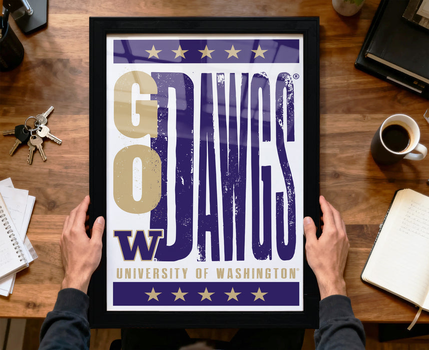 A framed poster with the text "GO DAWKS" is being held by a person's hands, with a wooden desk and various items such as keys, a coffee cup, and a notebook in the background.