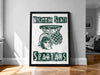 A framed poster with the Michigan State Spartans logo and a basketball net, displayed on a wall in a room.