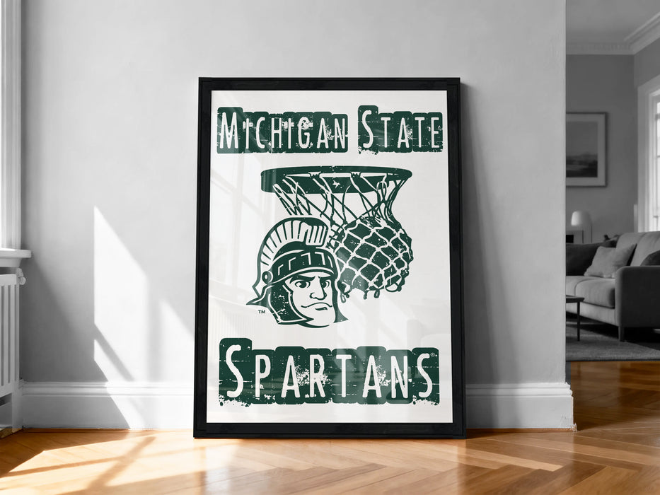 A framed poster with the Michigan State Spartans logo and a basketball net, displayed on a wall in a room.