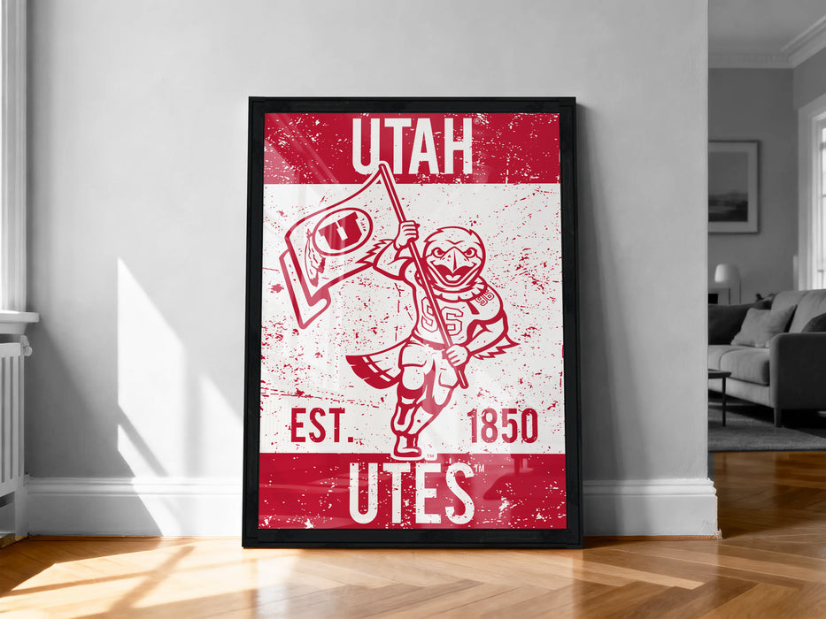 A framed poster of a red and white design featuring a bird-like character holding a flag, with text that reads "UTAH EST. 1850 Utes".
