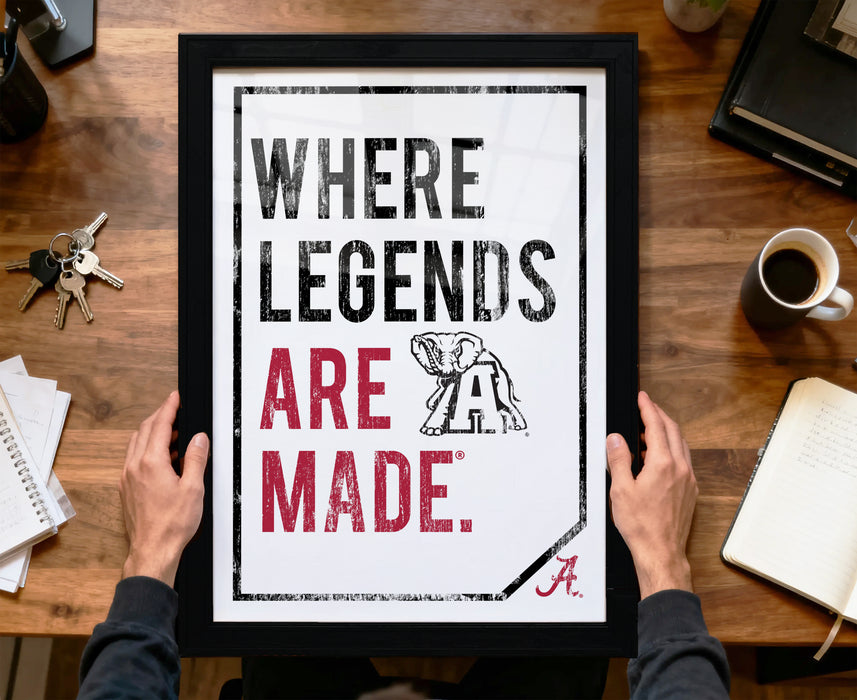 A person is holding up a framed poster with the text "WHERE LEGENDS ARE MADE" and an illustration of an elephant.
