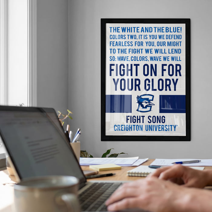 a framed poster with a motivational message on a wall, with a laptop and a person's hands visible in the foreground.