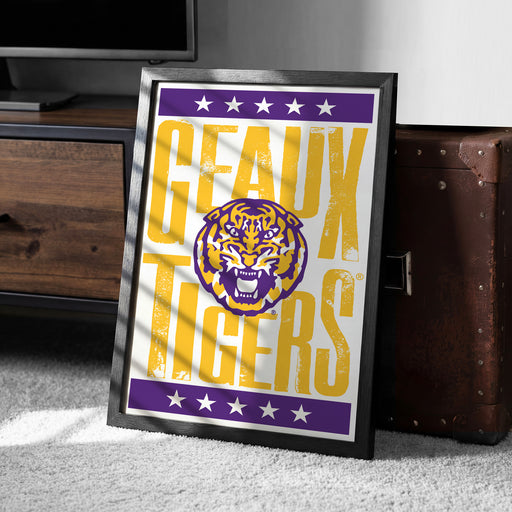 A framed poster with the text "GEAUX TIGERS" and a tiger logo, placed on a carpeted floor next to a wooden chest.