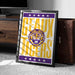 A framed poster with the text "GEAUX TIGERS" and a tiger logo, placed on a carpeted floor next to a wooden chest.